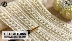 a crocheted white sweater next to flowers and a knitting needle on a wooden table