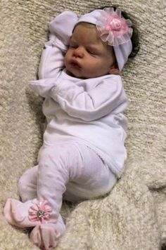 a baby laying on top of a blanket wearing a white outfit and pink bow tie