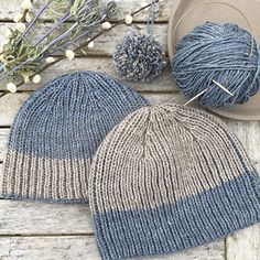 two knitted hats sitting on top of a wooden table next to a yarn ball