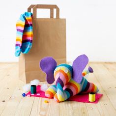 an elephant stuffed animal laying on the floor next to a bag and sewing thread,