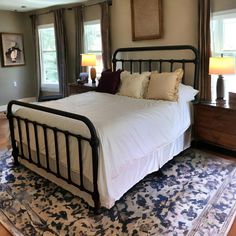 a bed with white sheets and pillows on top of a blue rug in a bedroom