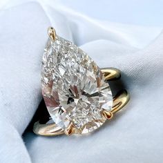 a pear shaped diamond ring sitting on top of a white cloth covered pillow with a gold band