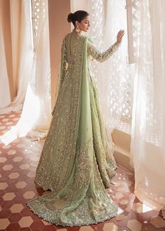 a woman standing in front of a window wearing a long green dress with intricate embroidery on it