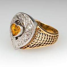 This captivating 18K yellow gold ring is topped a platinum gallery accented with one (1) heart mixed cut natural yellow sapphire set into a platinum bezel. The sapphire is bordered with nineteen (16), bead set, round brilliant cut diamonds. The top half of the 18K yellow gold shank features a pierced design. The ring measures 17.1mm at the top, rises 7.1mm above the finger, tapering to 4.6mm wide and 0.9mm thick at the base of the shank. Anniversary Yellow Sapphire Jewelry With Polished Finish, Collectible Yellow Gold Sapphire Ring With Diamonds, Yellow Rings With Polished Finish For Anniversary, Yellow Sapphire Ring With Center Stone For Anniversary, Luxury Yellow Sapphire Ring For Anniversary, Heart Cut Yellow Jewelry For Anniversary, Yellow Heart Cut Jewelry For Anniversary, Luxury Yellow Sapphire Anniversary Ring, Elegant Yellow Sapphire Ring For Anniversary