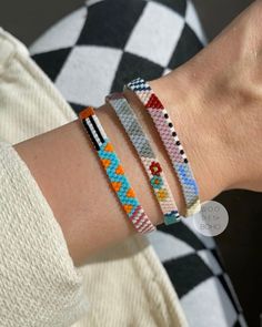 a woman wearing three different bracelets on her arm and one has an orange, white, blue, and green beaded design