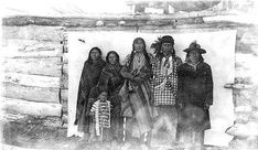 black and white photograph of people standing in front of a log cabin with snow on the ground