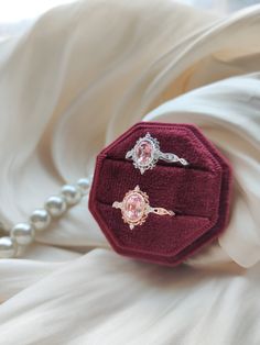 two rings sitting on top of a red velvet ring box next to a pearl necklace