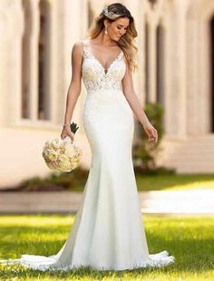 a woman in a white wedding dress walking through the grass with flowers on her hand