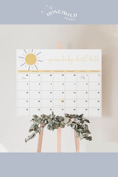 a desk calendar sitting on top of a wooden easel with greenery around it