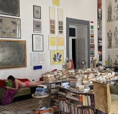 a woman laying on top of a couch next to a pile of books in a living room