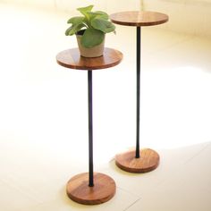 two wooden tables with black metal legs and a potted plant on each one side