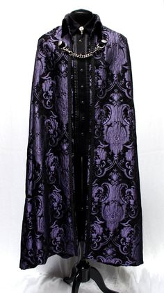 "A magnificent cape fit for royalty. Made in rich flowing black and gold tapestry fabric with rich black satin lining inside. The high pointed collar can be worn down or up for an extra dramatic effect. Braided black trim lines the collar and along the front of cape. Fully lined in rich black satin. Fastens in front with a heavy antiqued chain which clasp at either side to heavy D-rings and decorated with two ornate metal buttons. Slits in the front of cape allow the wearer to reach through and Wizard Aesthetic Outfit, Fantasy Suit, Prince Cape, Cloak Outfit, Purple Cape, Black Tapestry, Black Cloak, Gold Tapestry, King Outfit