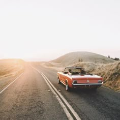 an old car is driving down the road in front of some hills and sand dunes