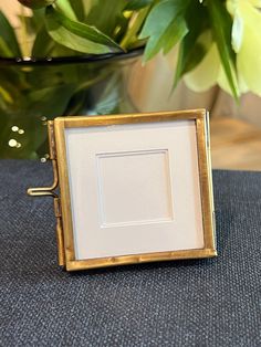 a small square frame sitting on top of a table next to a potted plant