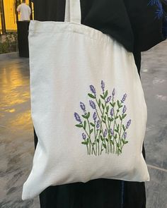 a person holding a white bag with purple flowers painted on the front and side of it