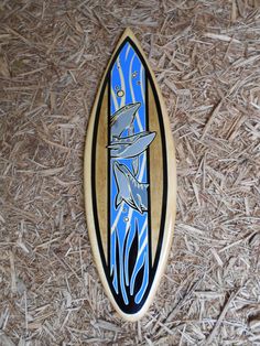 a wooden surfboard sitting on top of some dry grass and straw with an image of two dolphins swimming in the water