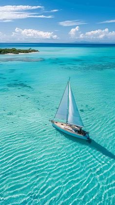 a sailboat floating in the middle of clear blue water with an island in the background