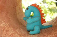 a blue toy with an orange head and tail sitting in a clay bowl, looking up at the ground