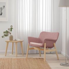 a pink chair sitting next to a small table on top of a rug in front of a window