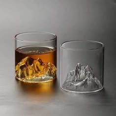 two glasses filled with liquid and ice on top of a gray table next to each other