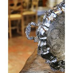 an ornate silver plate sitting on top of a piece of wood in front of a dining room table