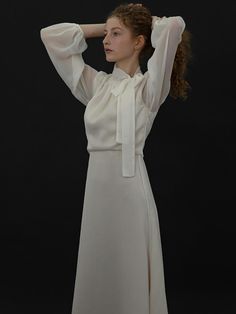 a woman in a white dress with her hands on her head and looking off to the side