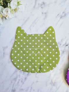 a green and white cat shaped placemat on a marble surface with flowers in the background