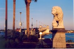 a statue of a lion is in front of the water and street lamps on either side