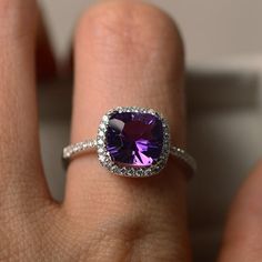 a close up of a person's hand holding a ring with a purple stone