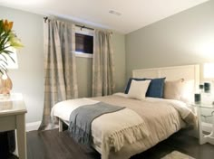 a white bed sitting next to a window with curtains on top of it and a vase filled with flowers