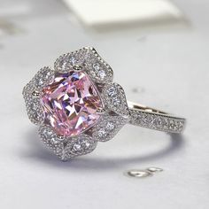 The Platinum Plated Sterling Silver Ring, Cushion Super Light Pink CZ Stone Milgrain Vintage 2 carat Engagement Ring, Pink Diamond Simulant Ring Cocktail Ring (Size 5 to 9) is nothing short of breathtaking. With its vintage-style vibe, it showcases an eye-catching light pink cushion cut cubic zirconia encircled by sparkling round cut accents set in milgrain edge finish petals being formed a heart shape. It would be a sensation at a garden party and a lovely complement to your little black dress Pink Topaz Ring With Halo Setting As Gift, Pink Cubic Zirconia Halo Ring For Wedding, Pink Heart-shaped Rings For Formal Occasions, Pink Topaz Promise Ring In Fine Jewelry Style, Classic Pink Cluster Ring For Anniversary, Pink Topaz Ring For Promise, Fine Jewelry Style, Pink Topaz Promise Ring With Prong Setting, Pink Crystal Promise Ring With Prong Setting, Pink Topaz Center Stone Ring For Anniversary