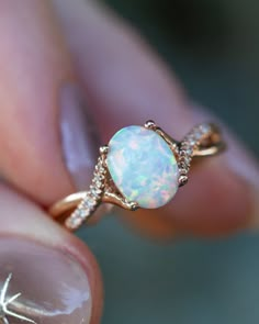 a woman's hand holding an opal and diamond ring