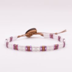 a white and pink beaded bracelet with brown leather cord on a white table top