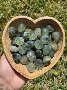 a heart shaped wooden bowl filled with lots of green stones on top of a grass covered field