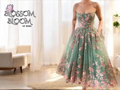 a woman in a green dress standing next to a white couch and window with the words blossom bloom on it