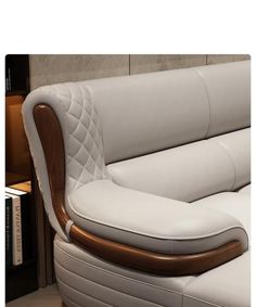 a white leather couch with wooden arms and foot rests on a table next to a bookcase