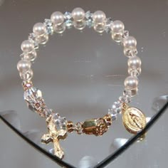 "This Catholic One Decade Rosary Bracelet is a perfect accessory for your little girl's First Holy Communion day! This bracelet is created using all Swarovski crystal and pearls. The Aves are 6mm white pearls. The Pater is an 8mm round crystal, surrounded by crystal rondelles. The spacers shown are 4mm clear or AB bicone crystals. Each rosary bracelet comes complete with a 3/4\" Crucifix, 1/2\" Miraculous Medal or Holy Communion charm. While this listing shows gold plate, please visit my Religio One Decade Rosary, Girly Bracelets, Decade Rosary, Wrist Jewelry, St Benedict, Rosary Bracelet, Jewelry Accessories Ideas, Dope Jewelry, Classy Jewelry