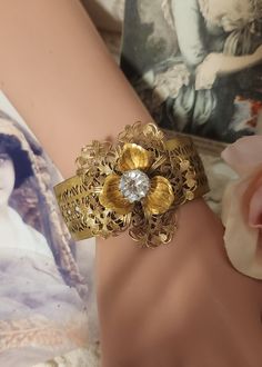 "This lovely one-of-a-kind vintage assemblage bracelet features beautiful layered vintage filigree flowers on a 1\" pierced vintage brass bracelet base. A large rhinestone vintage button is at the center of the flower. The bracelet is 6 1/2\" long, and bendable to size. It's a great gift for Christmas, a birthday or an anniversary....or just buy it for yourself.   I have included free insured First Class shipping within the USA which will take 4-5 days.  If you need faster delivery you can upgra Vintage Handmade Flower Jewelry, Unique Brass Bracelets For Wedding, Unique Brass Wedding Bracelets, Vintage Cuff Bracelet As A Gift, Vintage Metal Bracelet, Vintage Filigree Bracelet For Wedding, Vintage Filigree Bracelets For Wedding, Vintage Handmade Wedding Bracelets, Bohemian Gold Jewelry For Vintage Events