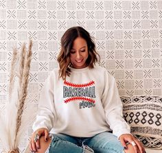 a woman sitting on a couch wearing a baseball mom sweatshirt