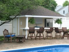 a backyard with a pool, table and chairs next to the swimming pool in front of it