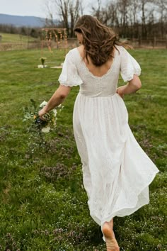 a woman in a white dress is walking through the grass