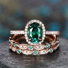 two wedding bands with an oval green stone surrounded by smaller emeralds and white diamonds