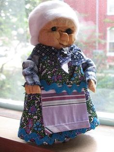 a teddy bear dressed in an old fashioned dress and holding a shopping bag on a window sill