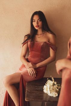 a woman in a red dress sitting on a wooden table next to a vase with flowers