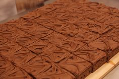 a square chocolate cake sitting on top of a wooden cutting board covered in frosting