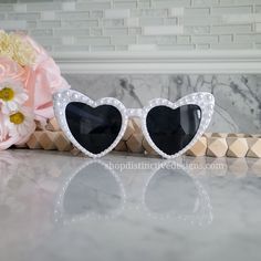 two heart shaped sunglasses sitting on top of a counter next to pink flowers and a vase