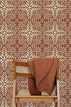 a chair with a blanket on top of it in front of a patterned wallpaper