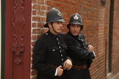 two police officers standing next to each other in front of a brick wall and red door