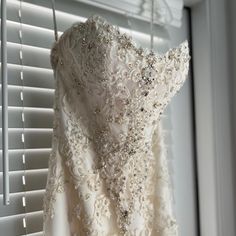 a wedding dress hanging on a rack in front of a window with white shutters