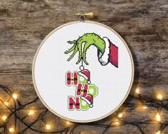 a cross stitch christmas ornament hanging from a string with lights around it on a wooden surface